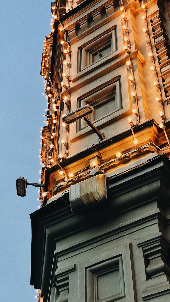 Vertical view of a decorated building facade with warm festive lights against a clear sky.