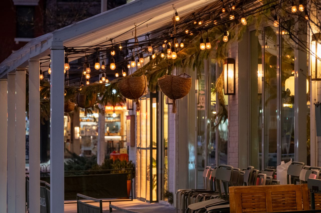 Warm and inviting café exterior in New York with festive lights and greenery.