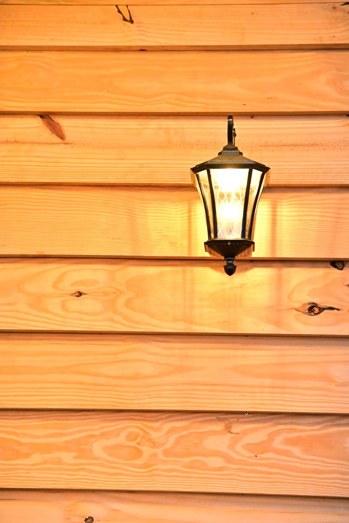 About A warm-lit wall lantern mounted on a polished wooden siding creates an inviting ambiance.