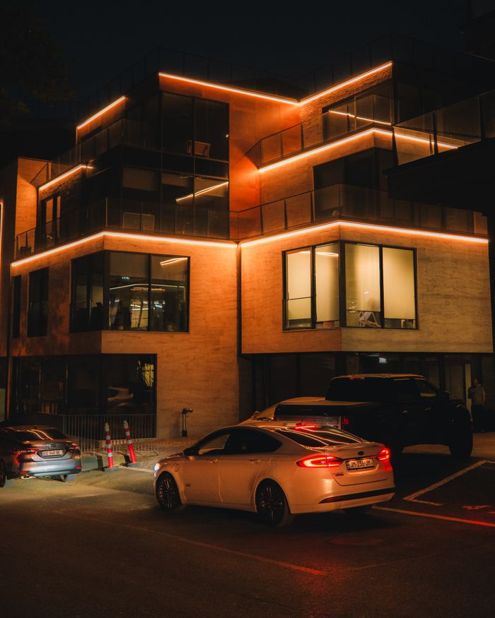 Night view of a modern building with vibrant lighting and parked cars.